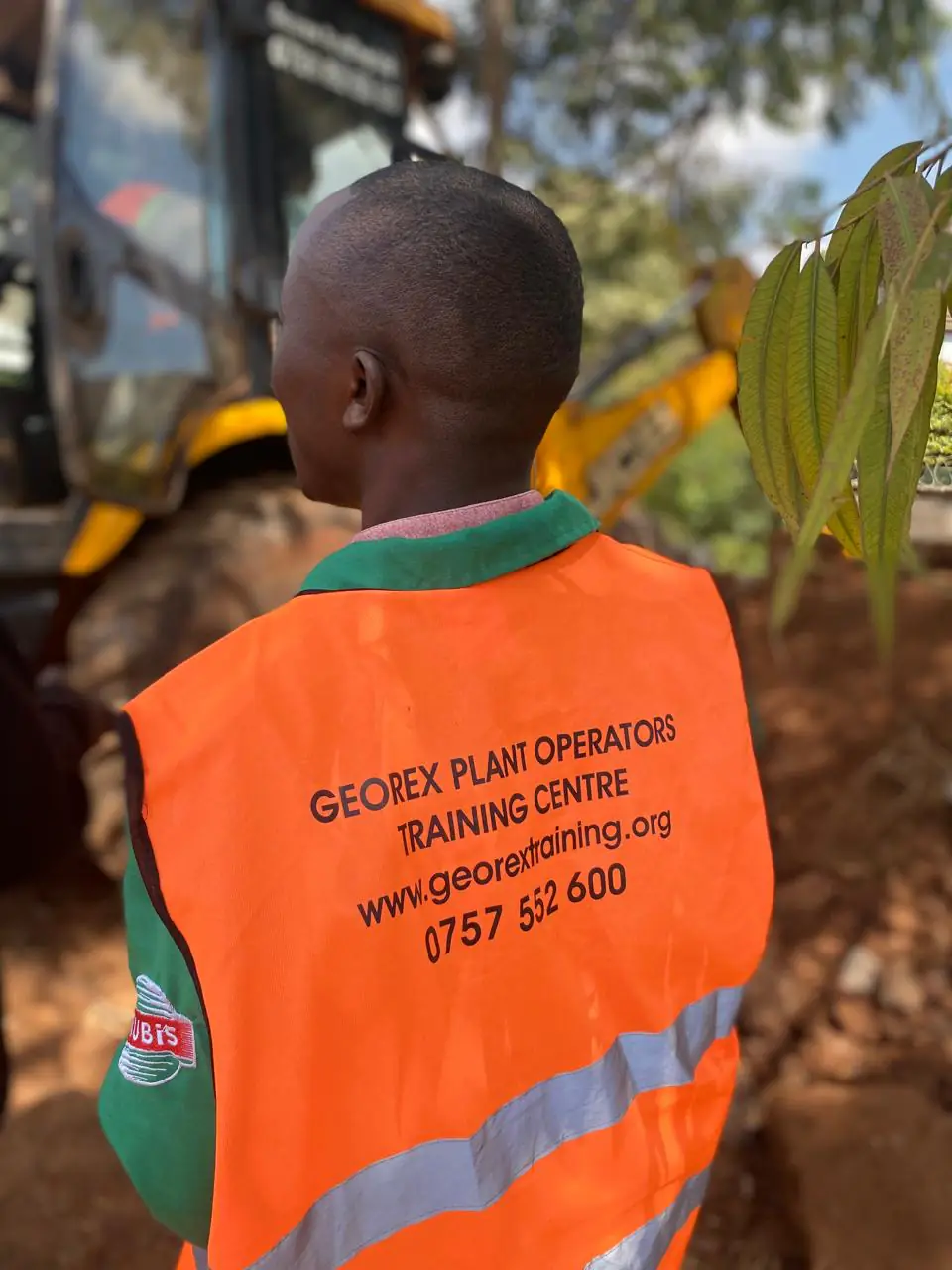 Georex trainee wearing branded high-visibility safety gear beside a backhoe loader