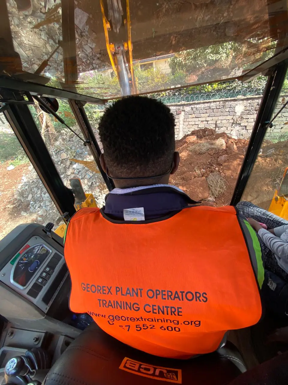 Over-the-shoulder view of practical instruction inside a JCB operator cab