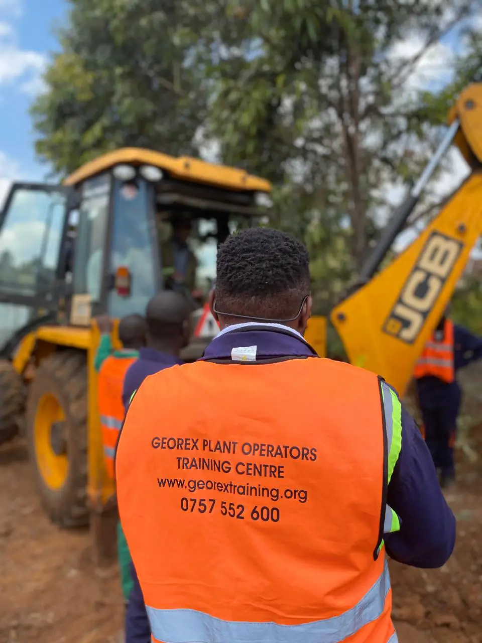 Georex instructor supervising trainees beside a backhoe loader